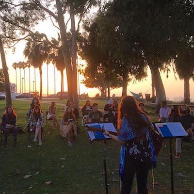Woman playing guitar with audience watching outside at sunset