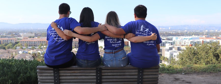 four students sitting on the bench overlooking the bluff with arms around each other