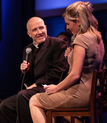 Fr. Bruce Morrill holding a microphone, speaking to a guest